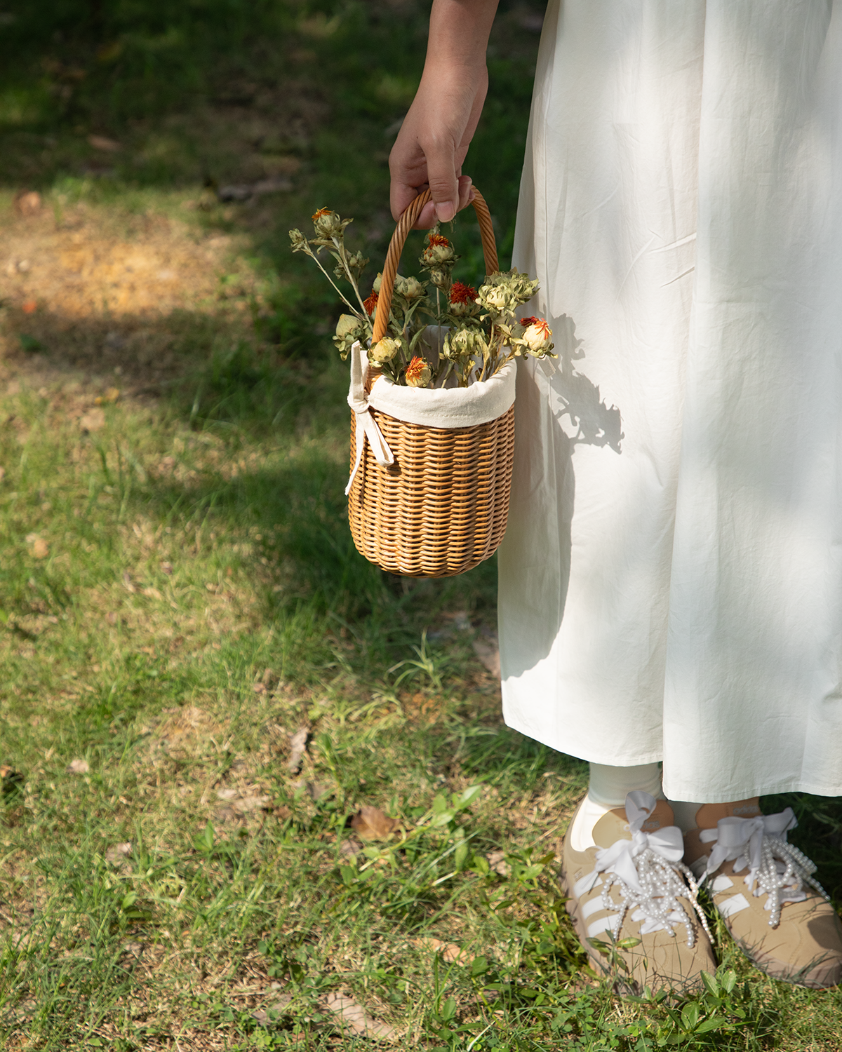Hand-woven cylindrical rattan Iris Basket with arched handle and cotton lining, holding dried flowers.