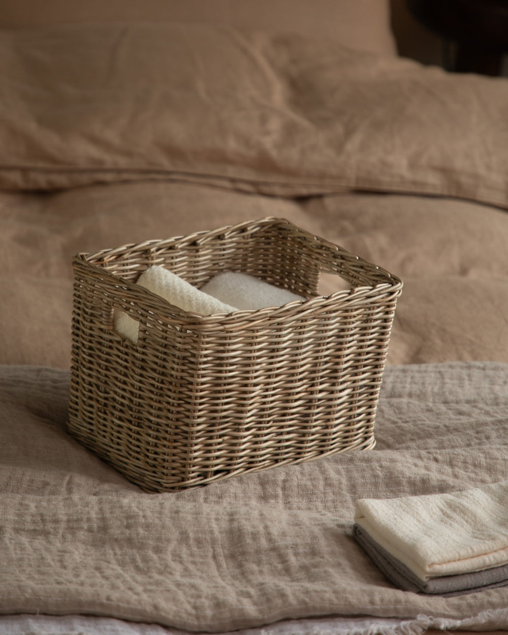 Loma Storage Basket: Woven natural fiber basket with handles holding folded towels, for home organization.