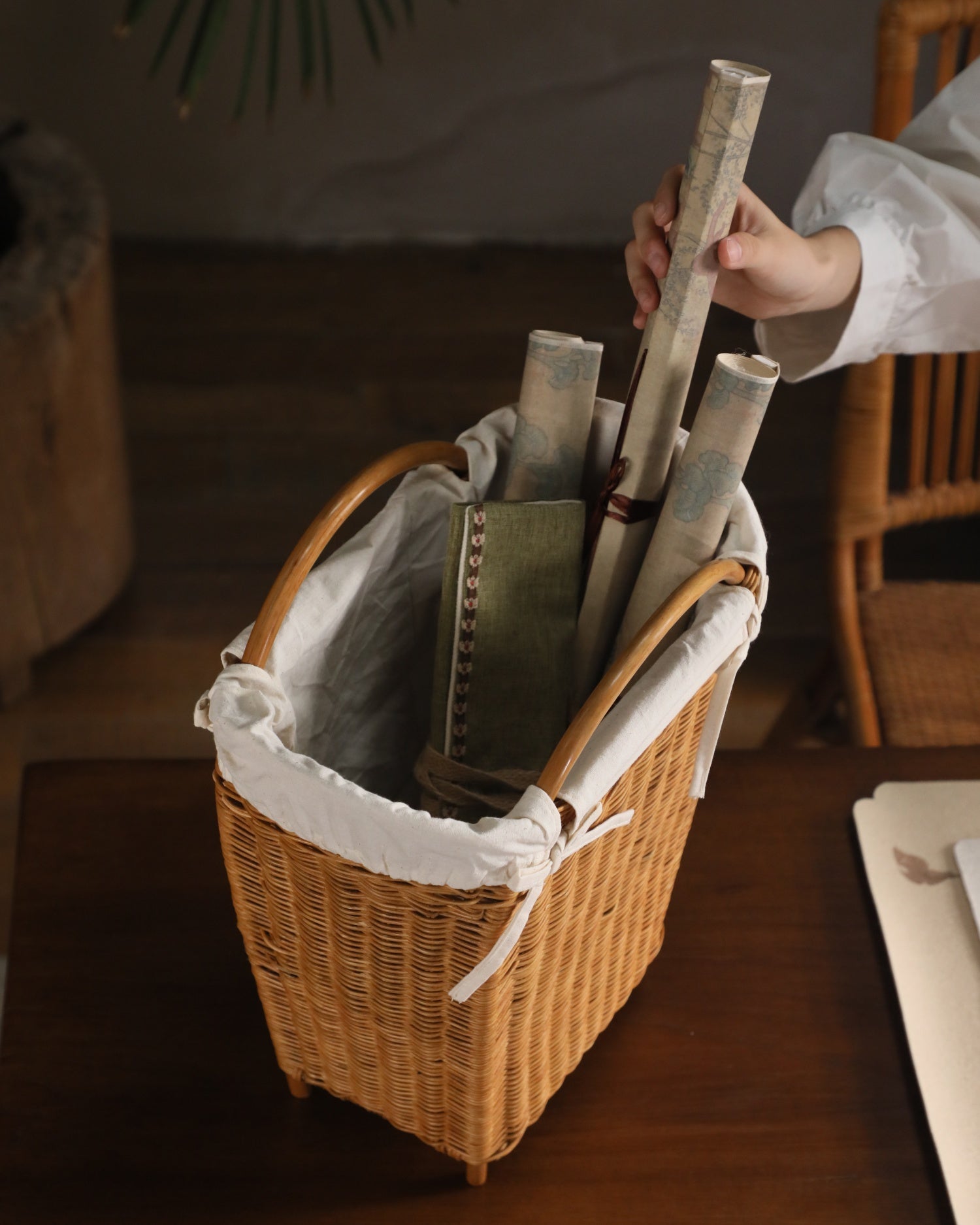 Woven rattan Luna storage basket with white lining, holding decorative scrolls and a notebook.