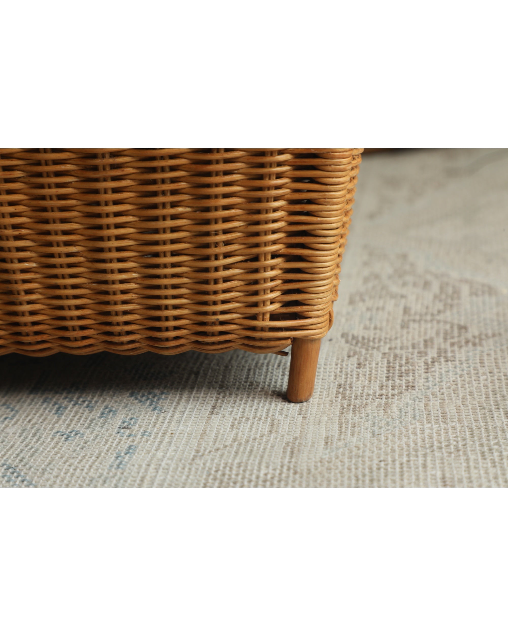 Luna Storage Basket close-up: intricately woven natural rattan base with a wooden leg on a textured rug.