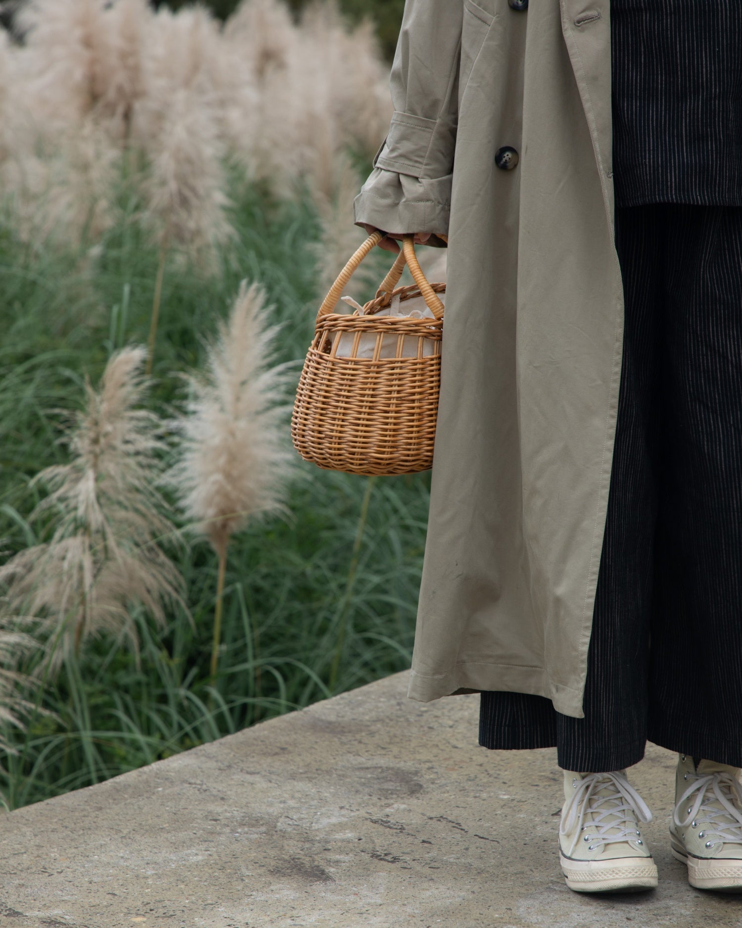 Ivy Hand Bag: Handcrafted woven rattan basket bag with pampas grass background.