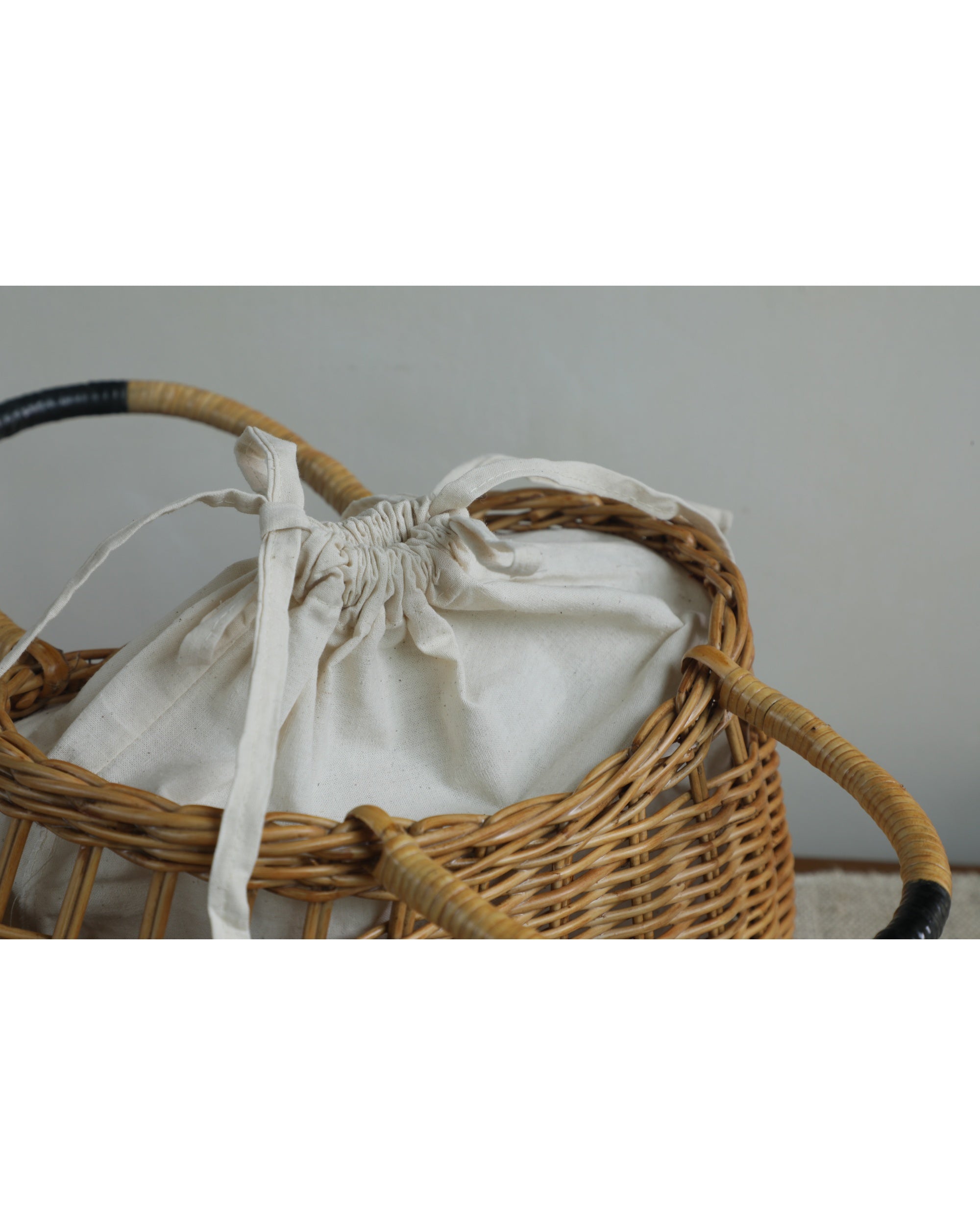 Woven rattan Ivy Hand Bag with a cinched white fabric liner and dark-wrapped handles.