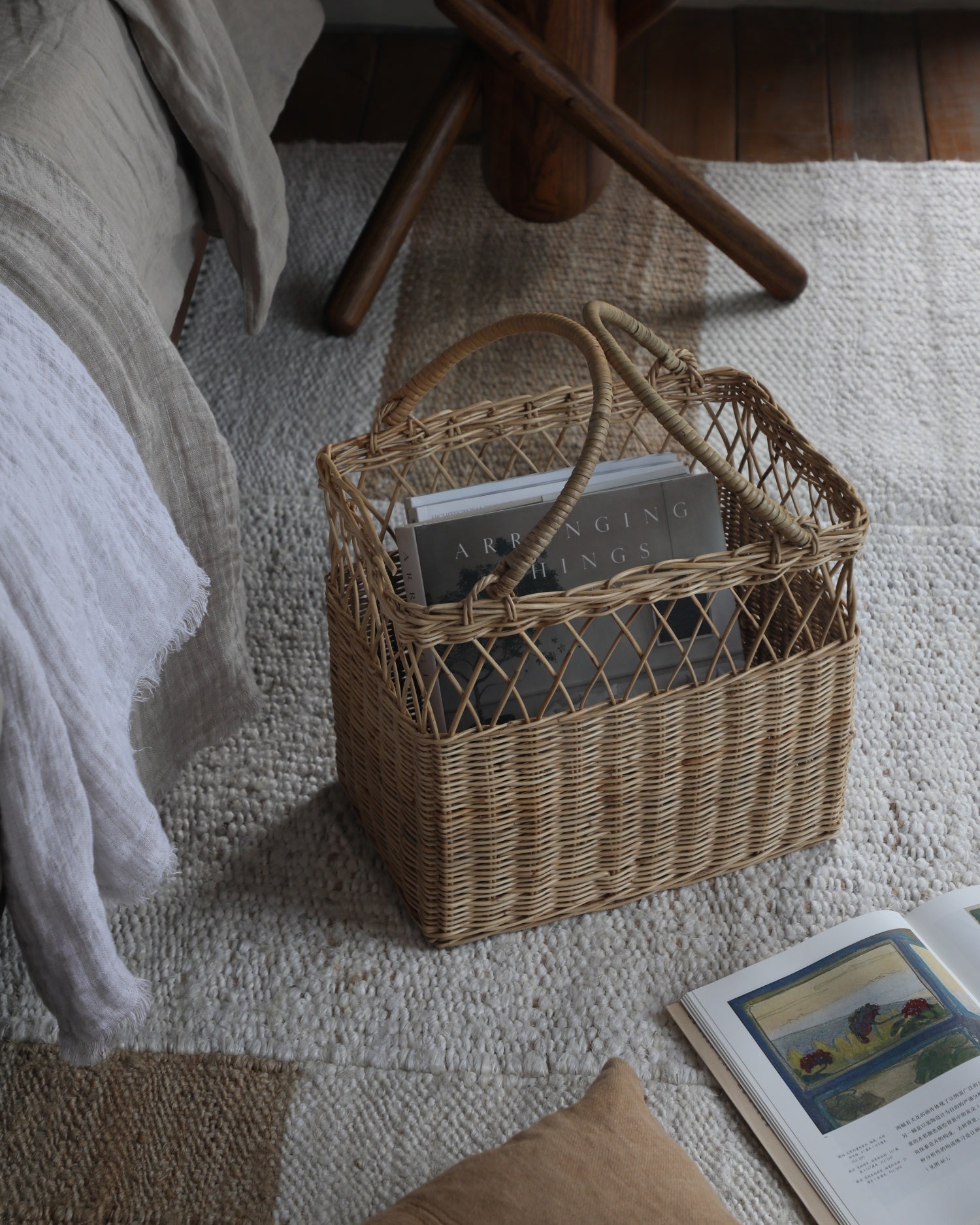 Lina Basket: Woven rattan basket with curved handles, holding 'Arranging Things' book.