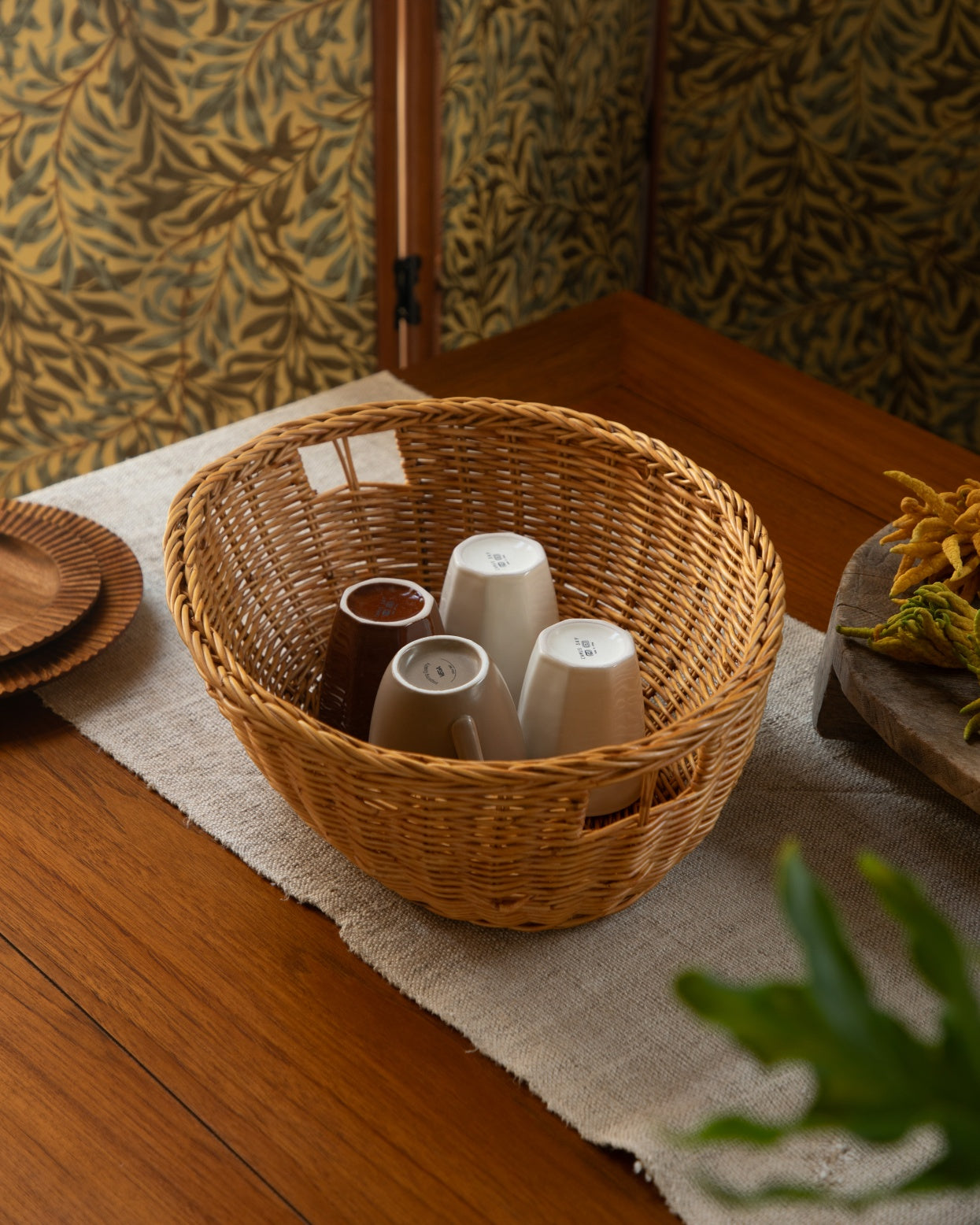 Dottie rustic woven rattan basket with neutral mugs on table.