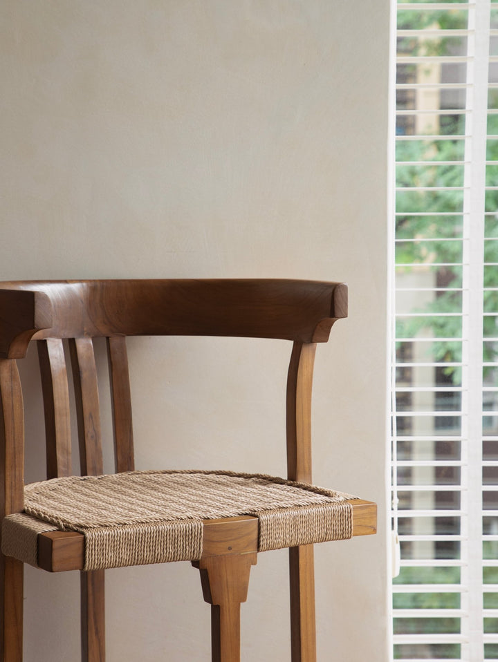 Elegant teak chair with woven seat against a backdrop of window blinds.
