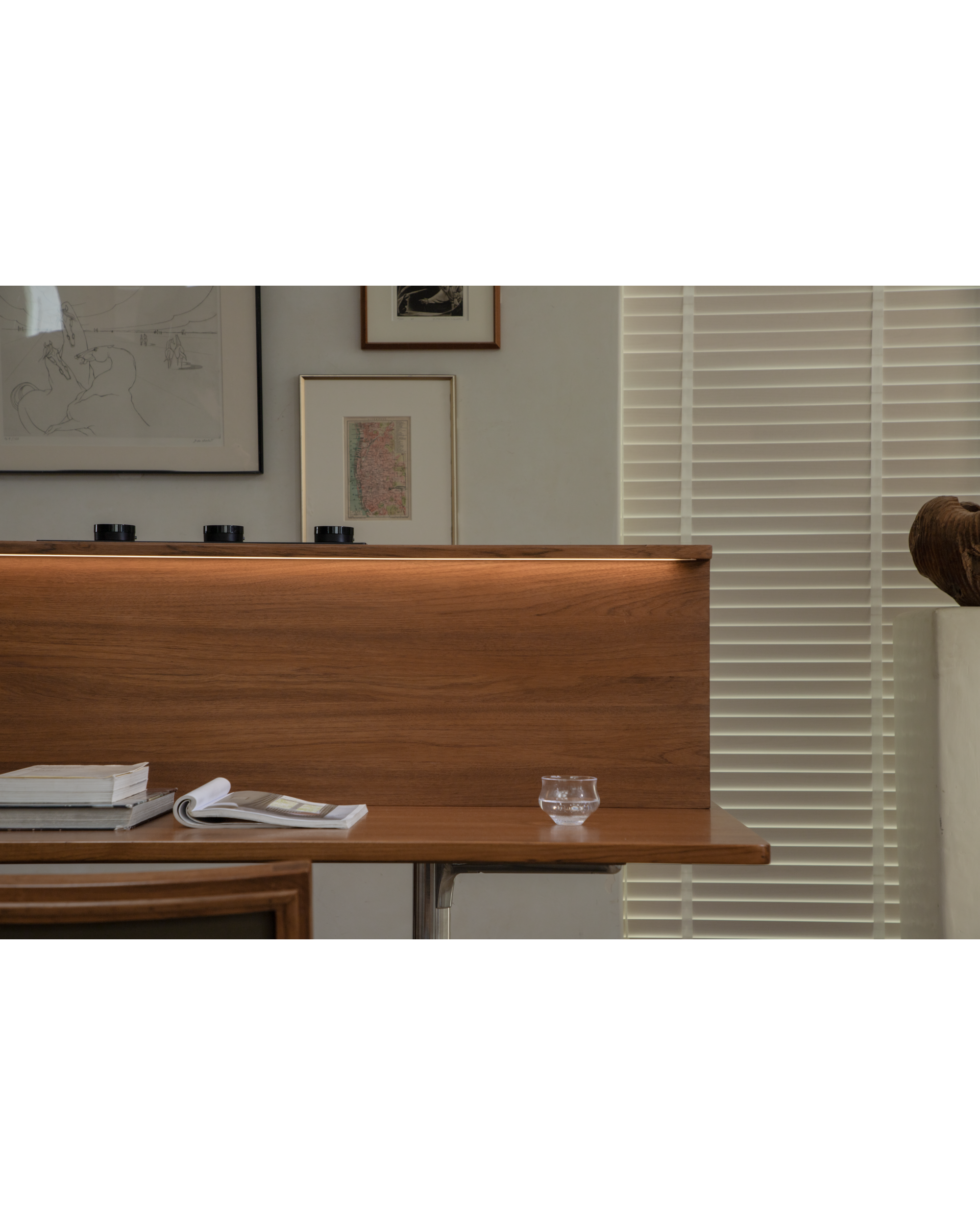Evan Office Desk detail: teak wood surface, books, water glass, ambient light.