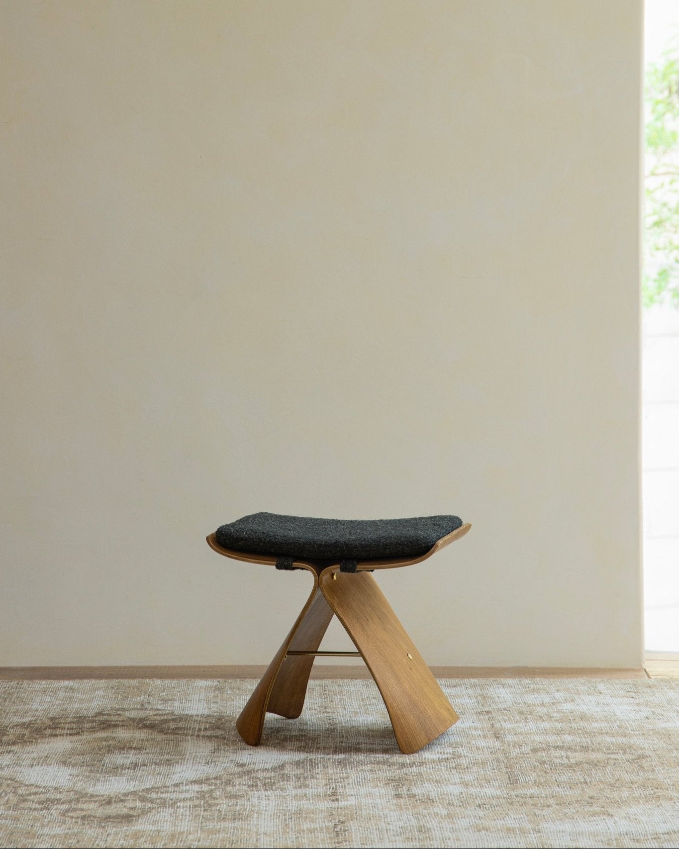 Butterfly Stool in natural wood finish with dark gray cushion, classic modern design, elegant seating