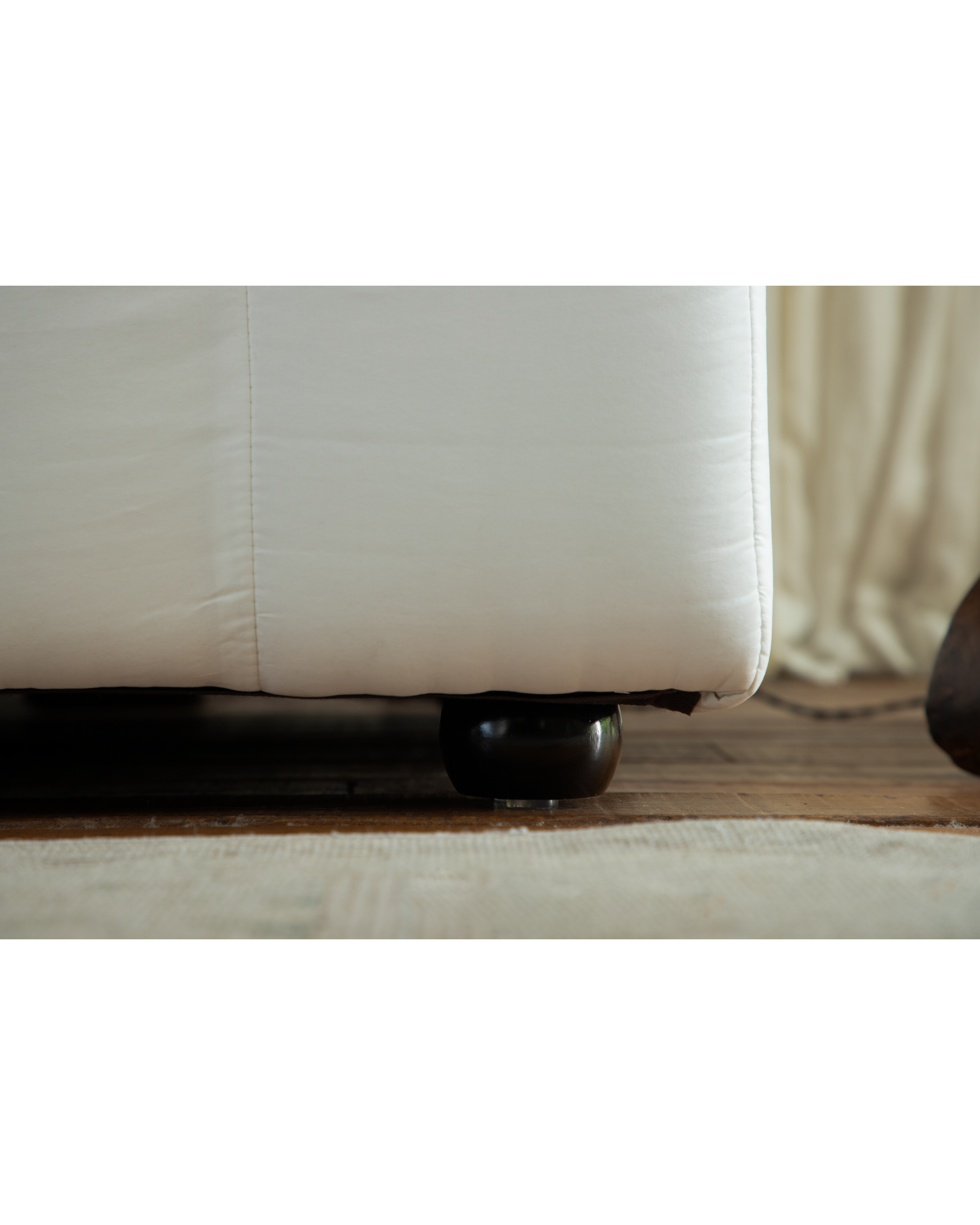 White Camille Sectional Sofa detail: dark polished round wooden leg on rug.