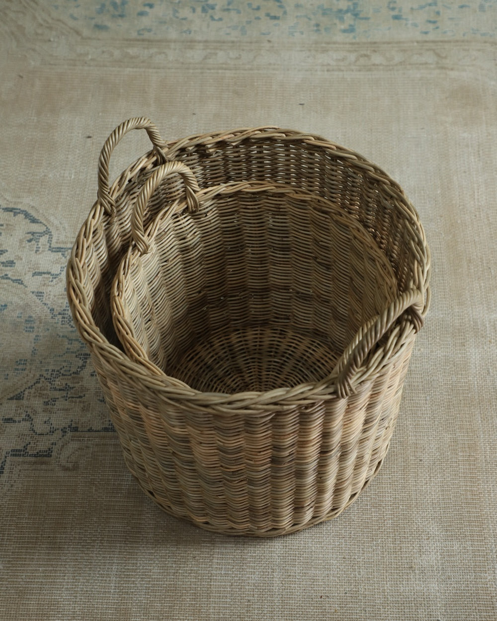 Two nested Aria round natural rattan storage baskets with woven handles.