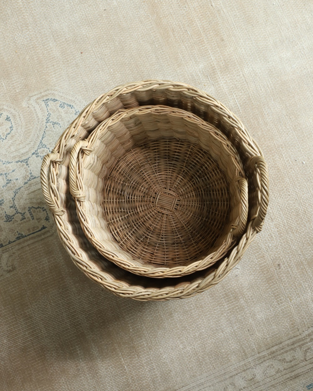 Two Aria round rattan storage baskets, hand-woven with natural material and handles.