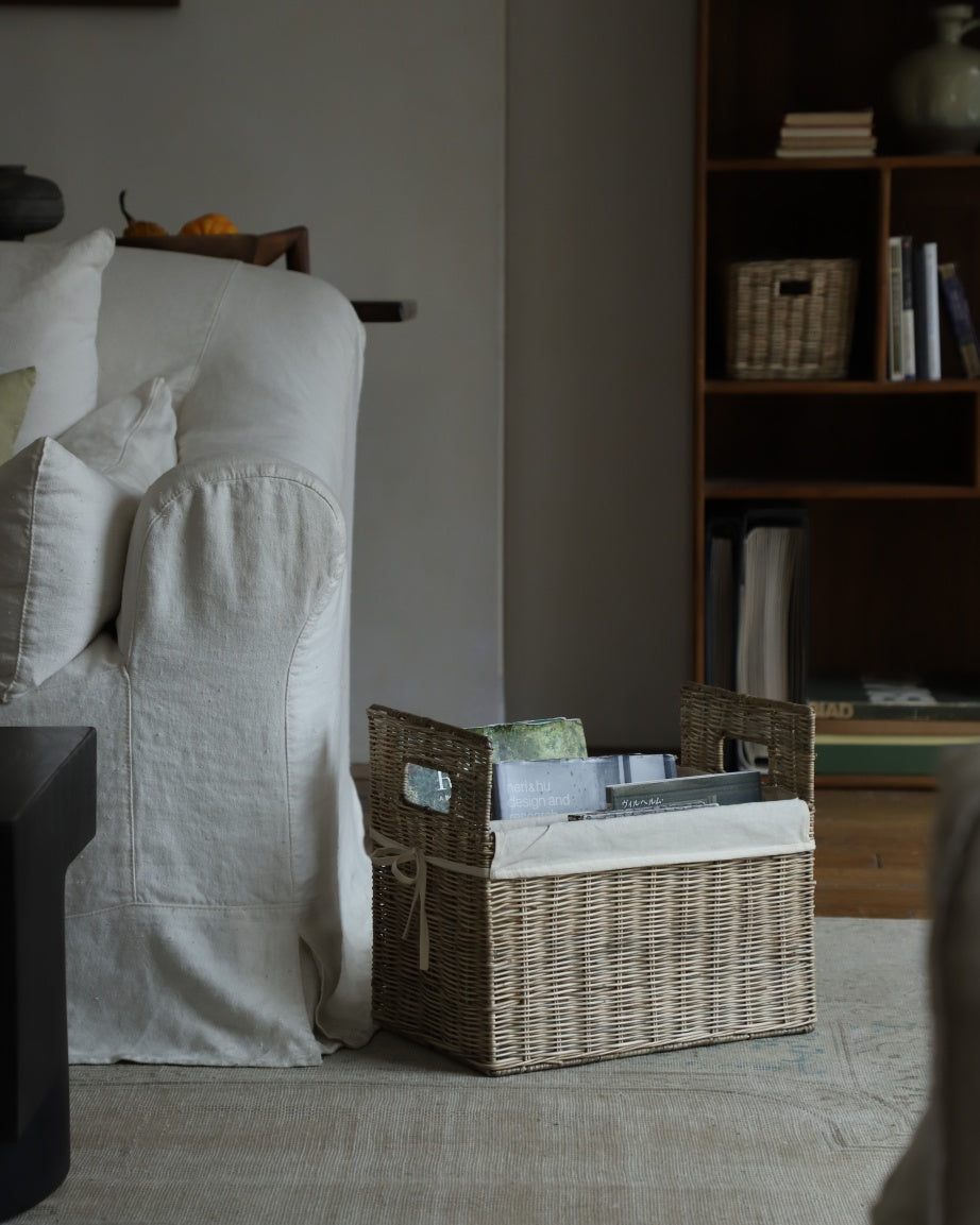 Elara Storage Basket made of woven natural rattan, holding books and magazines.
