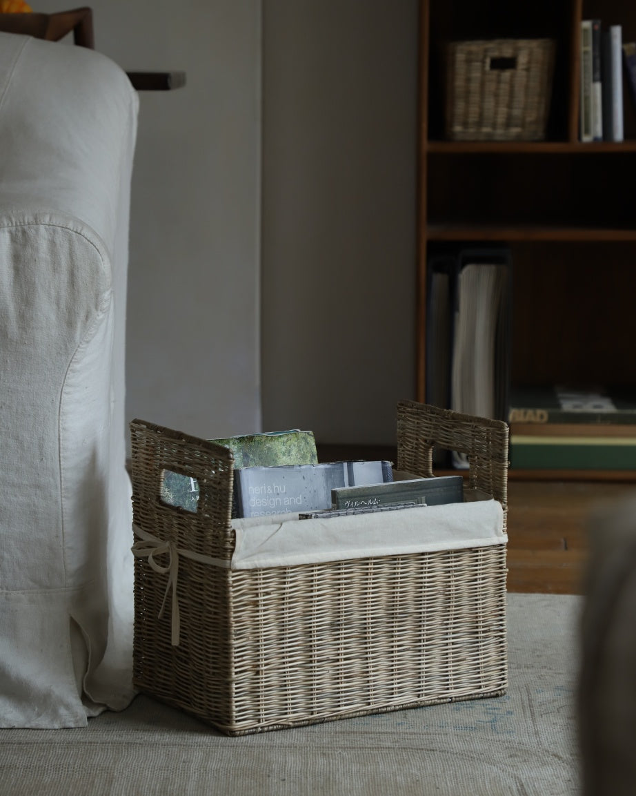 Elara woven rattan storage basket with handles, filled with books and magazines.