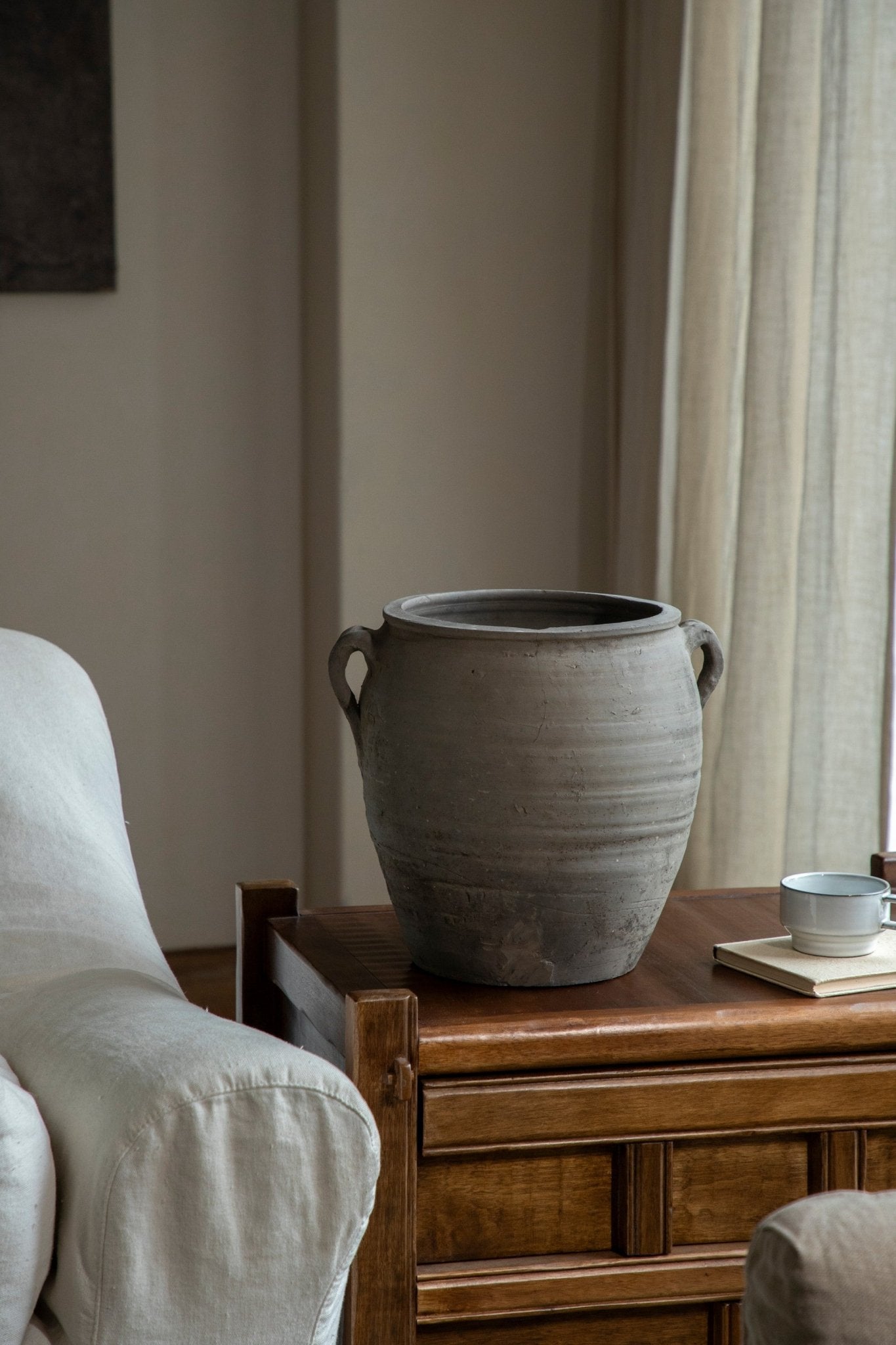 Large vintage clay pot with handles, home decor accent in neutral gray color, on wooden table with teacup.