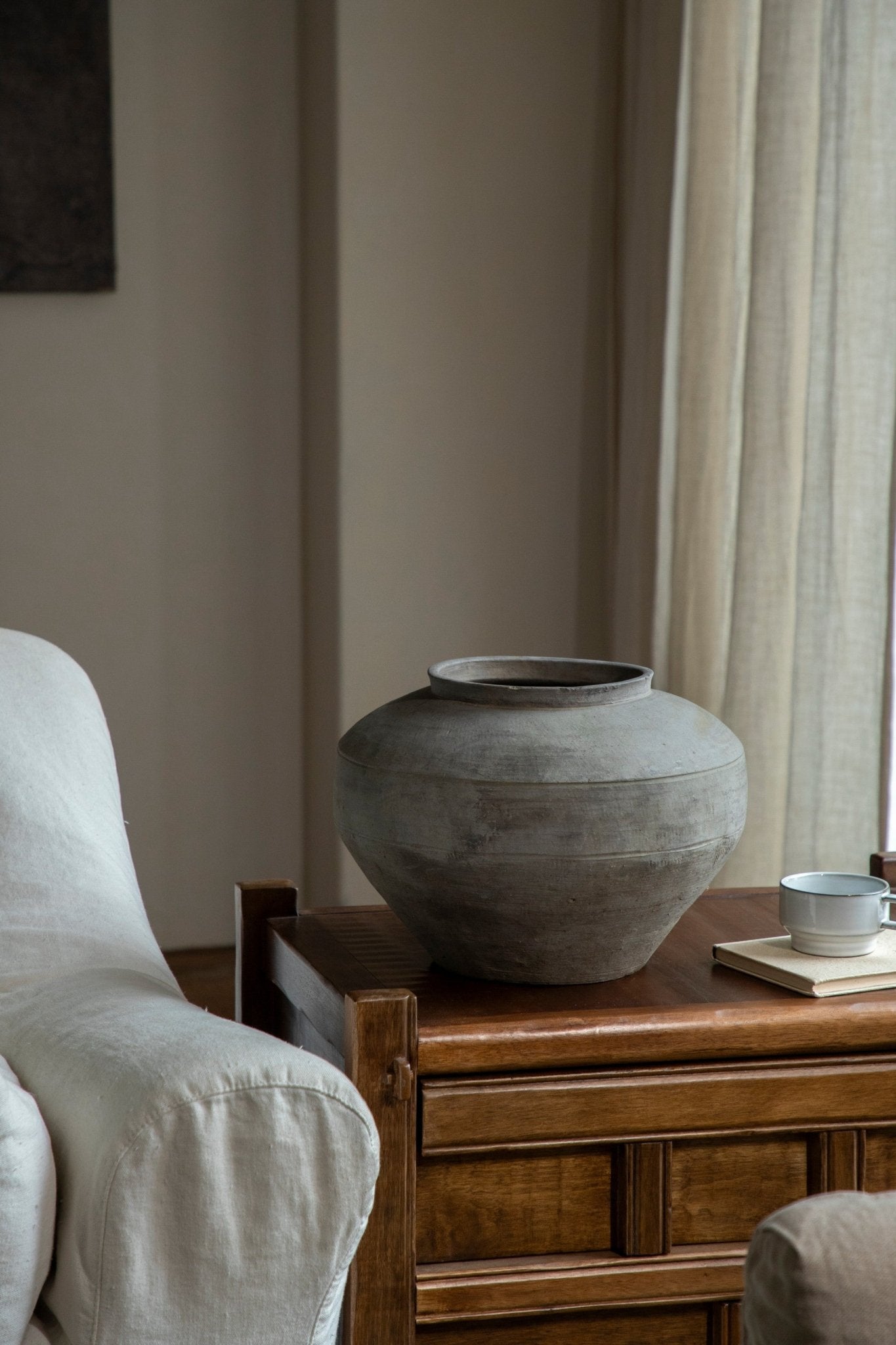Vintage clay pot, neutral gray, on a wooden table with teacup. Home decor accent, clay material.