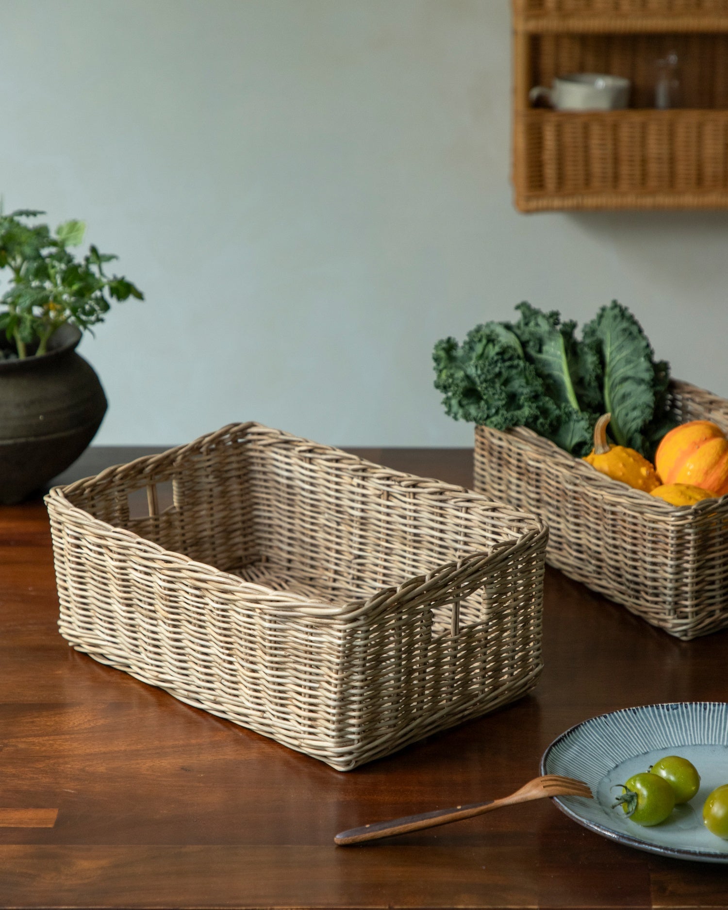 Etta storage basket woven from natural rattan, shown with vegetables on table.