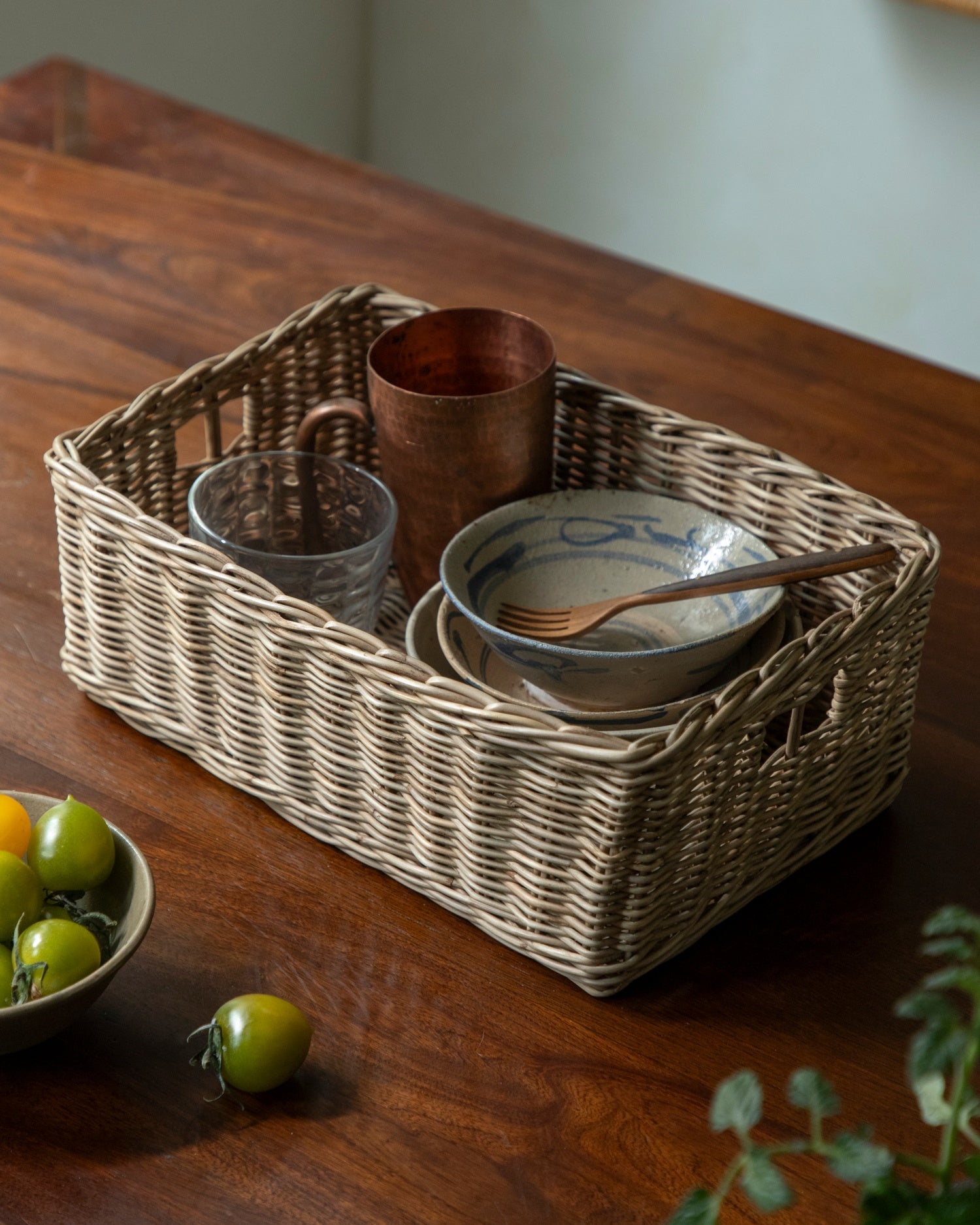 Etta woven storage basket of natural rattan, holding glasses, copper mug, and bowl.