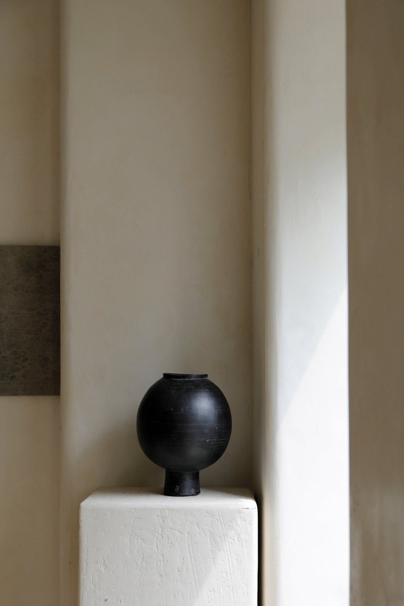 Black ceramic sphere vase on a white block, minimalist home decor