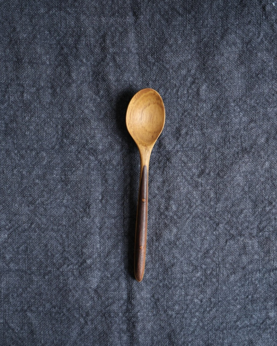 Ebony and teak wood handle table spoon on dark textured fabric