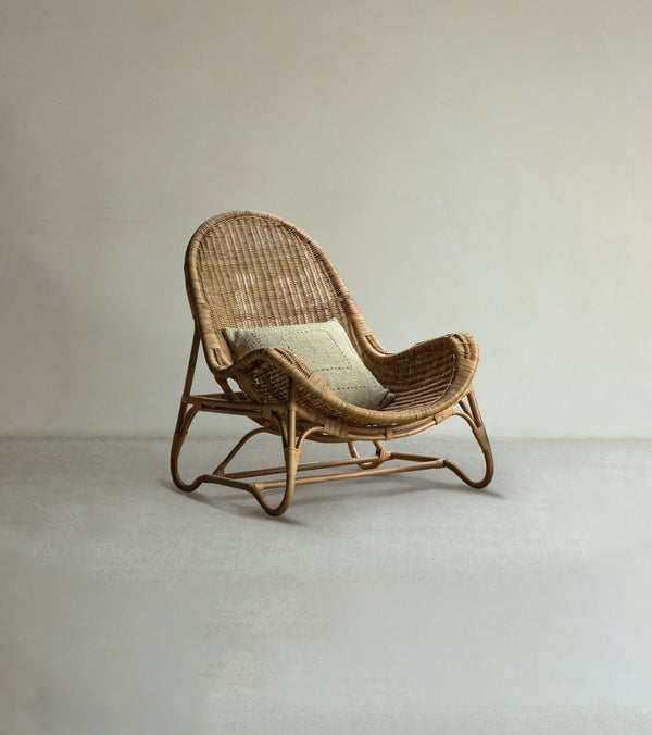 The Buffier Rattan Lounge Chair by ZM Home features a curved back and seat with a light green cushion, set against a beige wall on a plain floor—ideal for modern organic interiors.