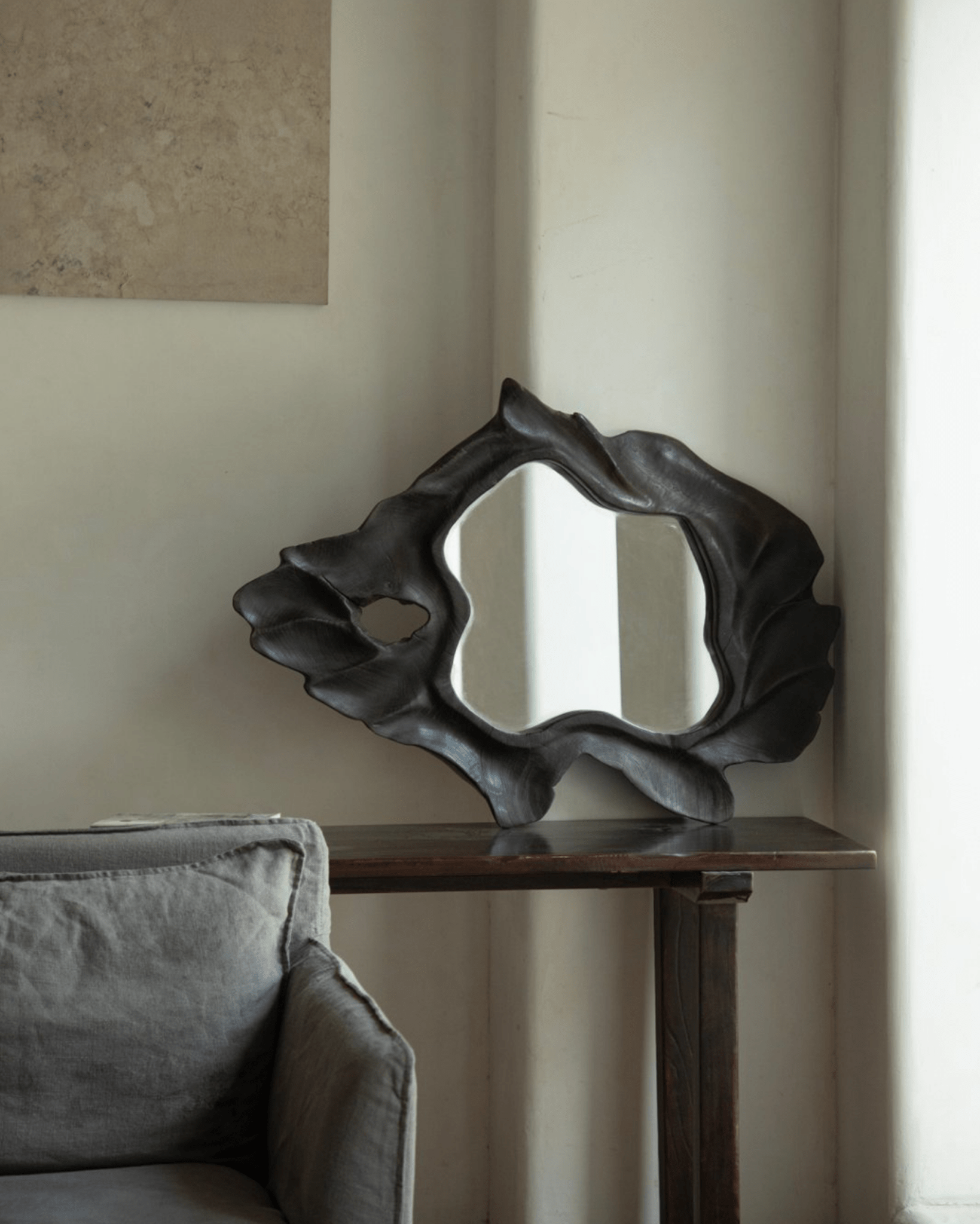 Organic Wood Arbor Mirror with dark finish, modern wall decor, natural shape, on a wooden table.