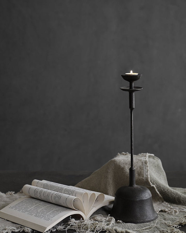 Elegant rustic iron candle holder beside an open book on a textured tabletop