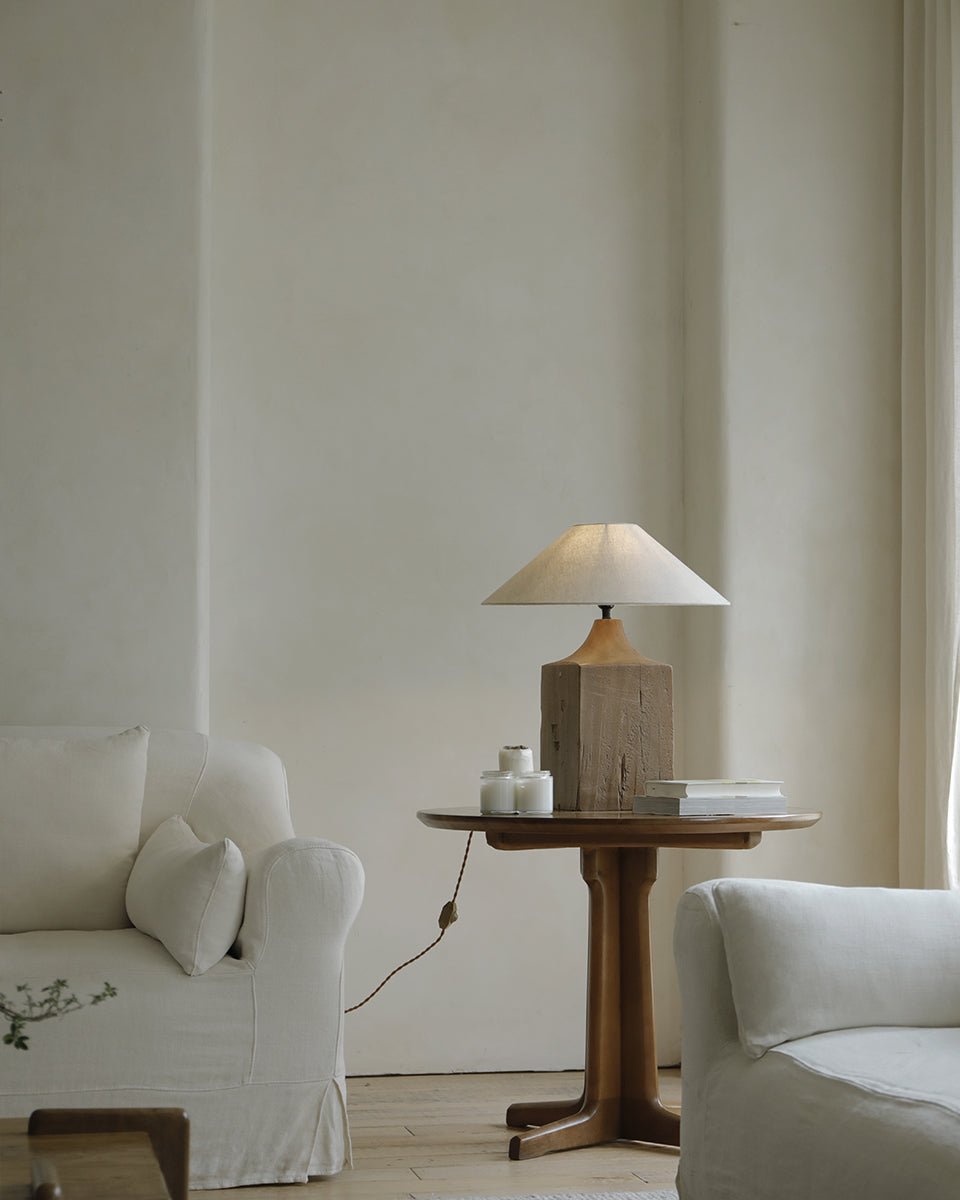 Wooden table lamp with a linen lampshade, placed on a small round wooden side table in a cozy living room setting