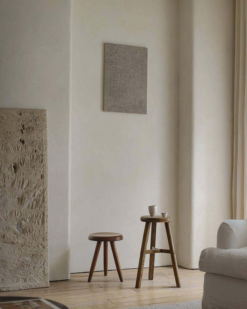 Minimalist room featuring two ZM Home Reclaimed Wood Vintage Chinese Stools, two white cups, a white armchair, a stone accent piece, and a neutral painting on a light-colored wall.