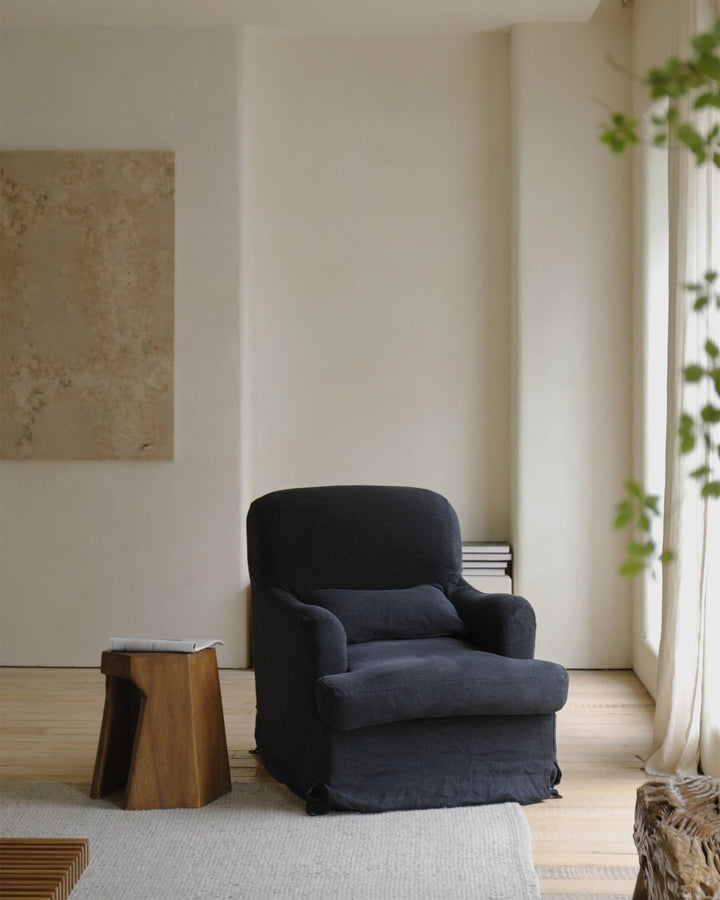 Dark slipcover armchair with cushion in a minimalist living space.