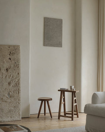 Vintage Chinese wooden stool with three legs beside reclaimed wood table in a minimalist room