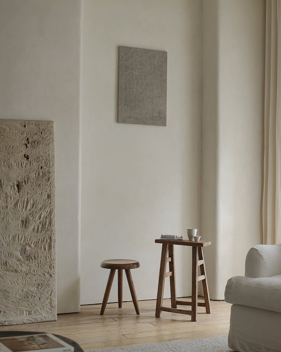 A minimal living room with a ZM Home Reclaimed Wood Vintage Chinese Stool, a small table set with cups and books, textured walls, and a white couch in softly lit surroundings.