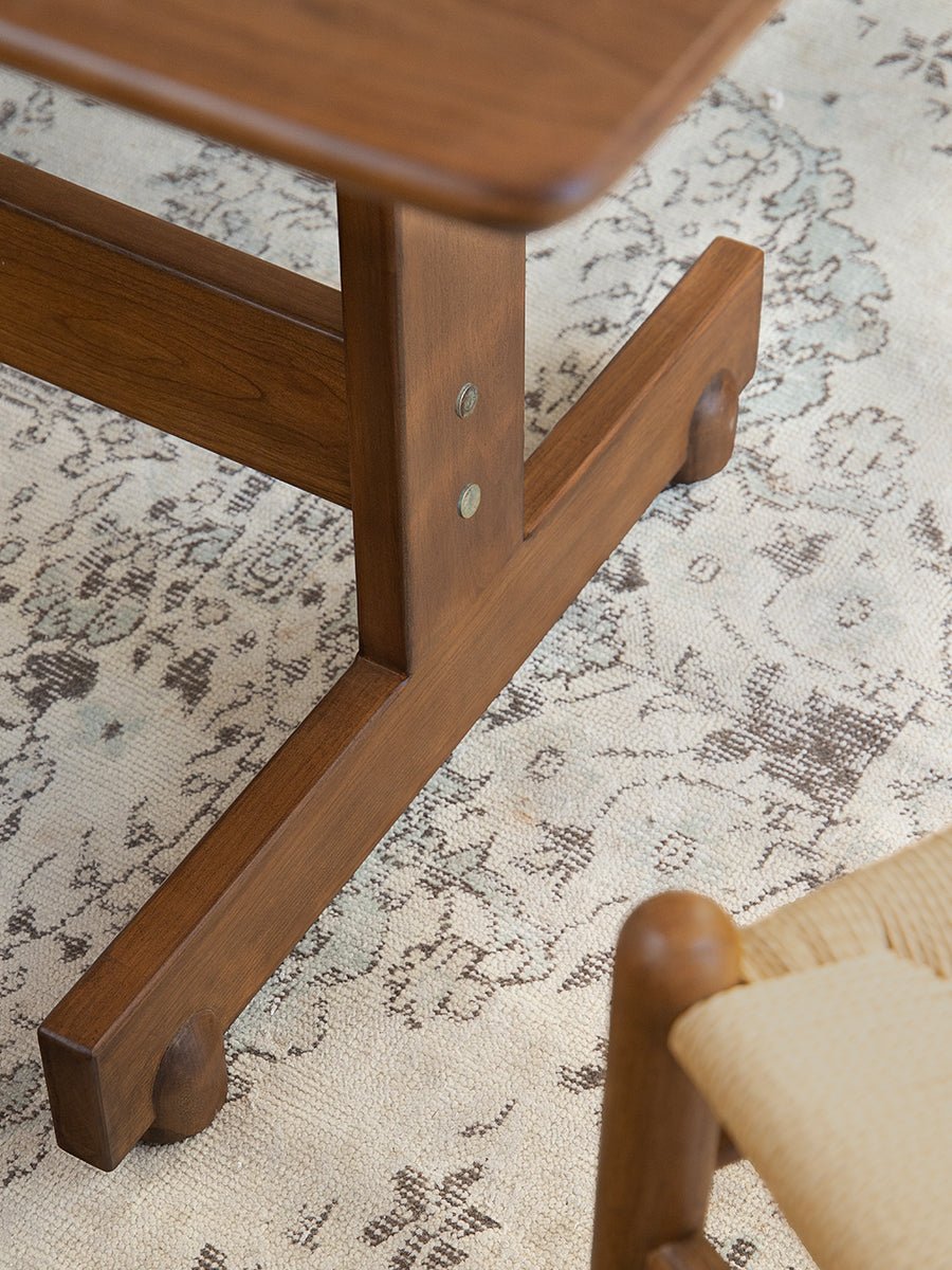 Hoof Dining Table's solid wood I-shaped base in warm brown finish, showcasing the table's stability and design.