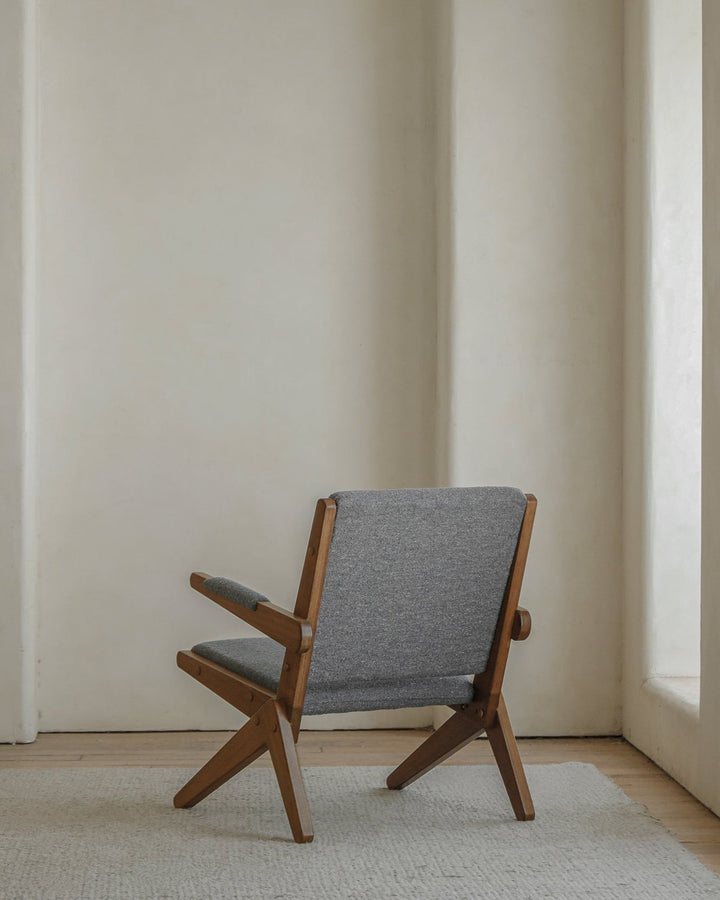 Scissors Chair with gray fabric upholstery and wooden frame in a minimalist setting