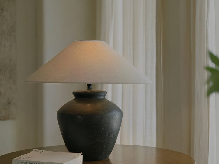 Elegant shirt lamp with a white shade atop a dark ceramic base on a wooden table.