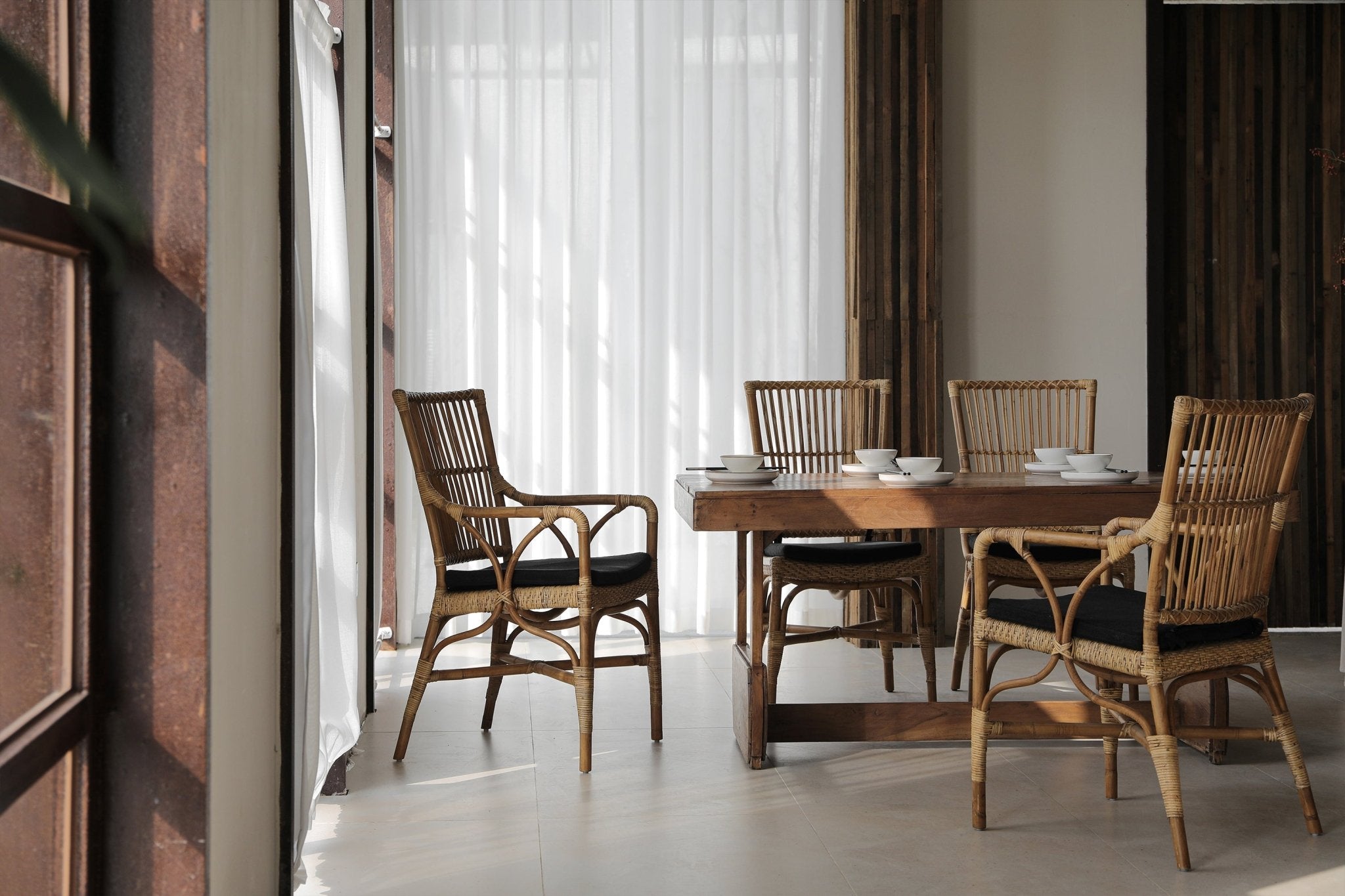Axis Chair dining set with Indonesian rattan chairs and black cushions in a neutral interior.