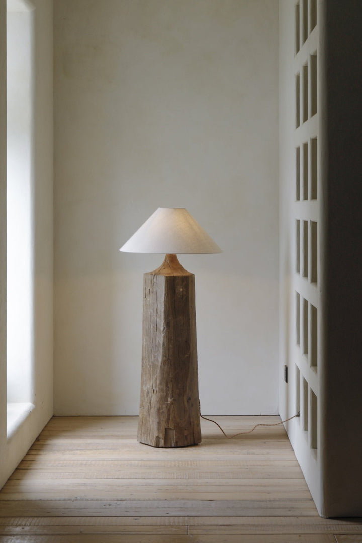 Earthy wooden floor lamp with conical shade illuminating a minimalist space.