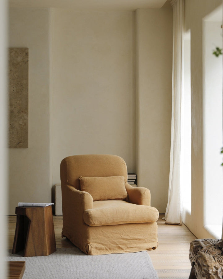 Caramel slipcover armchair with cushion in a sunlit, minimalist living room