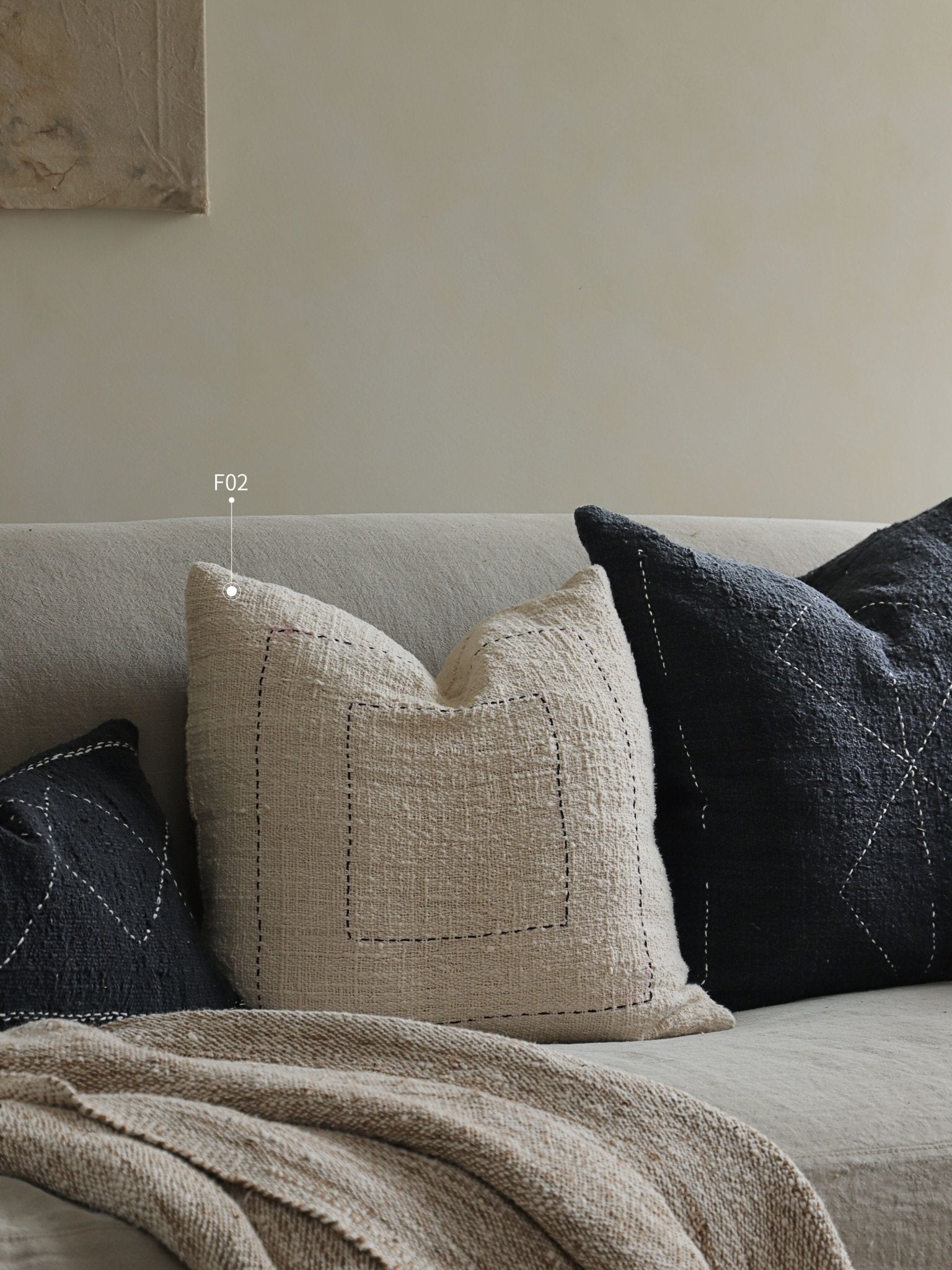Cotton pillows in neutral colors on a couch, featuring beige and black pillows with stitched designs, "F02".